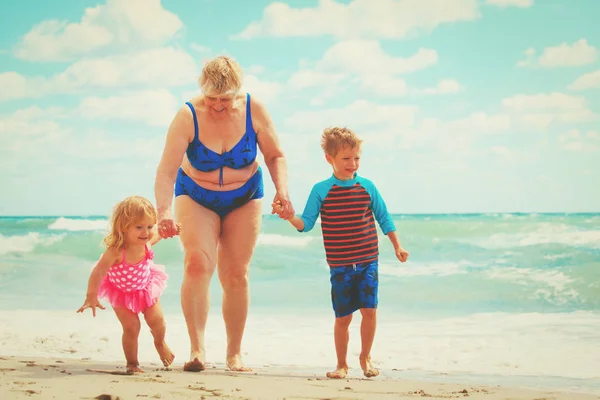Šťastná babička s dětmi - malý chlapec a dívka hra na pláži — Stock fotografie