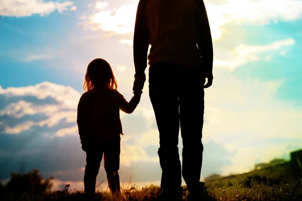 Silhueta de pai e filha de mãos dadas ao pôr do sol — Fotografia de Stock