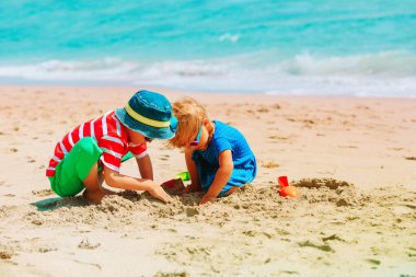 Küçük oğlan ve kız kumsalda kumla oynuyorlar.