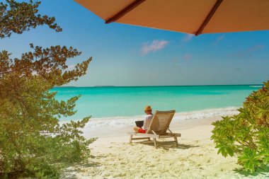 Kumsalda dizüstü bilgisayarda çalışan genç adam