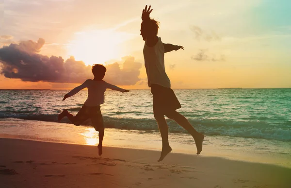 Pai e filho brincam, se divertem, pulam na praia do pôr do sol — Fotografia de Stock