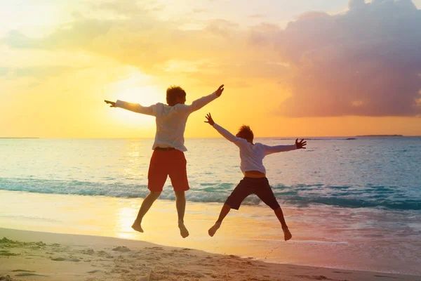 Father and son have fun jump at sunset beach — Stock Photo, Image