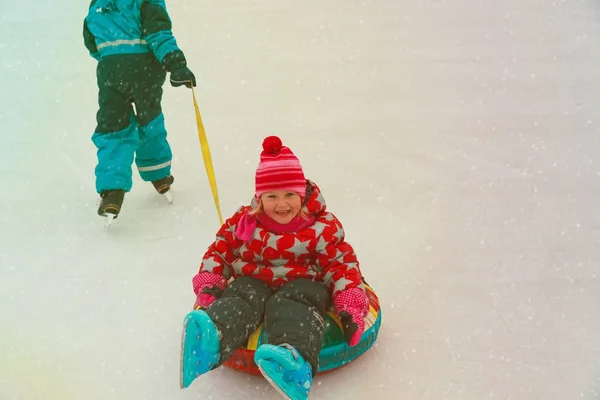 Petit garçon skate pousser heureux soeur dans tube, enfants hiver amusant — Photo