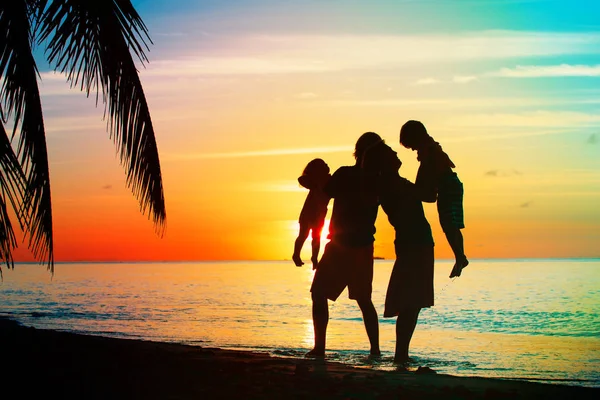 Glückliche Familie mit zwei Kindern spielt am Strand bei Sonnenuntergang — Stockfoto