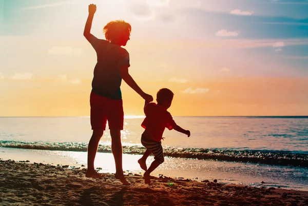 Vater und Sohn springen am Strand bei Sonnenuntergang — Stockfoto