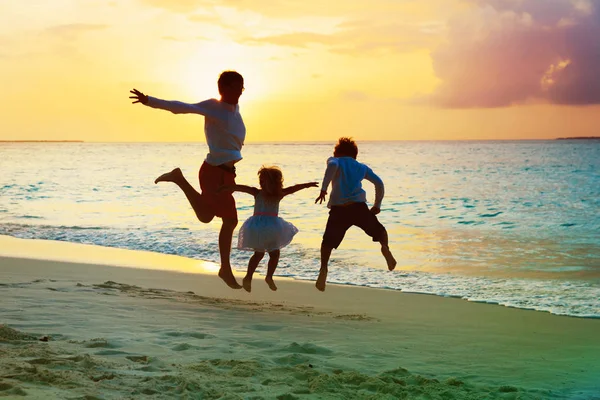 Vader en zoon en dochter hebben plezier springen op sunset beach — Stockfoto