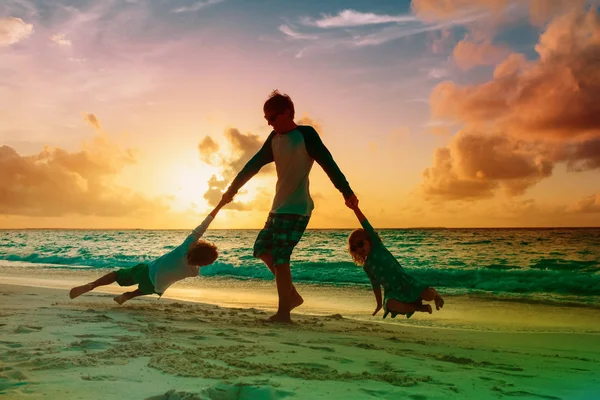 Vader en zoon en dochter silhouetten spelen op sunset beach — Stockfoto
