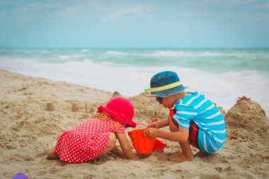 Küçük oğlan ve kız kumsalda kumla oynuyorlar.