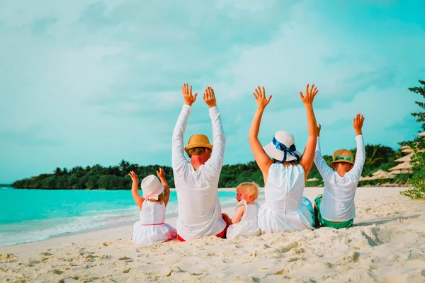 Gelukkige familie met twee kinderen handen omhoog op het strand — Stockfoto
