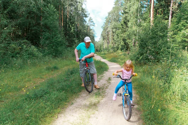Ativo sênior com neta andar de bicicleta na natureza — Fotografia de Stock
