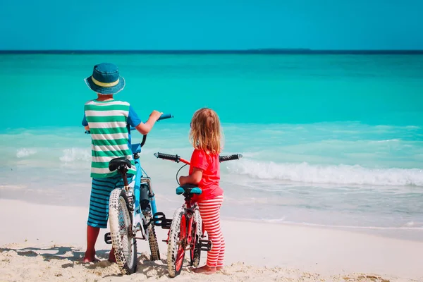 Liten pojke och flicka rida cykel på stranden — Stockfoto