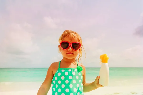 Koncepce opalování - holčička s opalovacím krémem na pláži — Stock fotografie