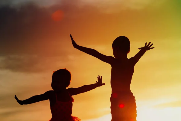 Petits garçons et filles silhouettes jouer au coucher du soleil ciel — Photo