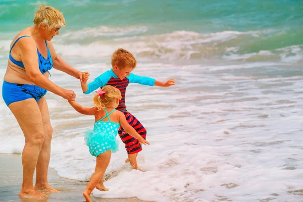 Gelukkig oma met kinderen - kleine jongen en meisje afspeelbare op strand — Stockfoto