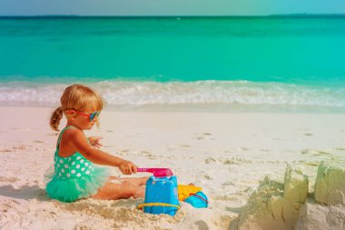 Tatlı küçük kız kumsalda kumla oynuyor.