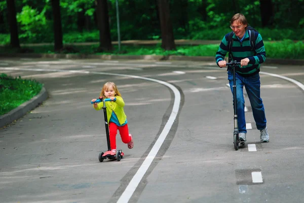 Маленькая девочка и отец на скутерах в городе — стоковое фото