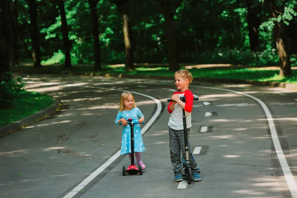 Dos niños niño y niña montando scooters en la ciudad —  Fotos de Stock