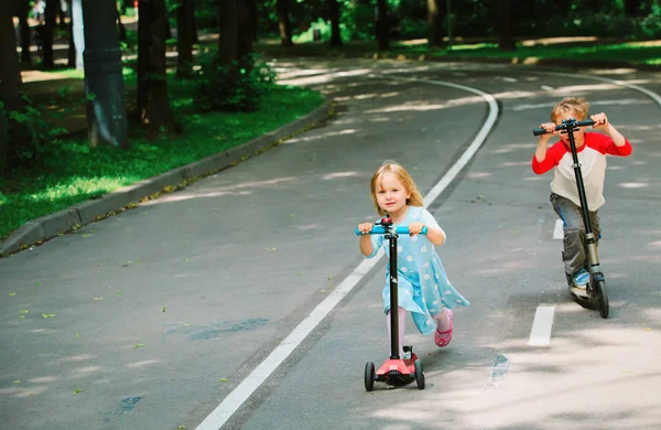Duas crianças menino e menina montando scooters na cidade — Fotografia de Stock
