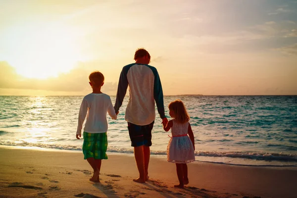 Vader en zoon en dochter lopen op het strand bij zonsondergang — Stockfoto