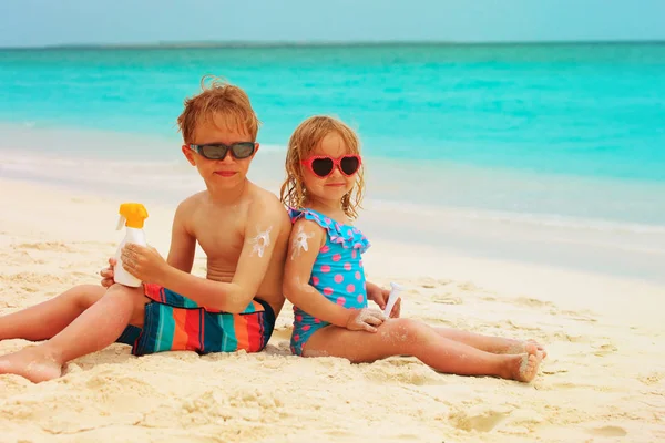 Sluneční ochrana - rád, malý chlapec a dívka s opalovací krém na pláži — Stock fotografie