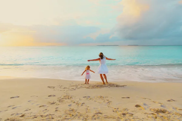 Glückliche Mutter mit kleiner Tochter spielt am Strand bei Sonnenuntergang — Stockfoto