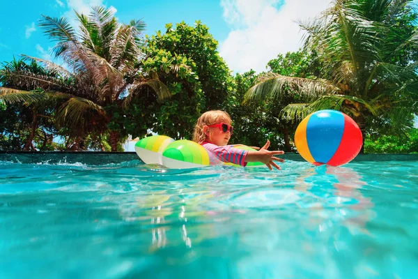 Kleines Mädchen spielt mit Ball schwimmen im Pool, Urlaubskonzept — Stockfoto