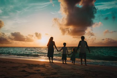 Çocuklu mutlu bir aile gün batımında sahilde yürüyor.