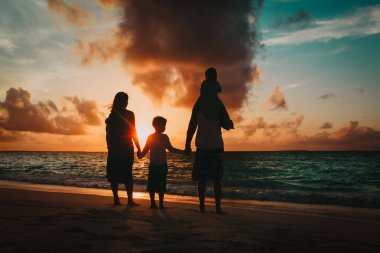 Çocuklu mutlu bir aile gün batımında sahilde yürüyor.