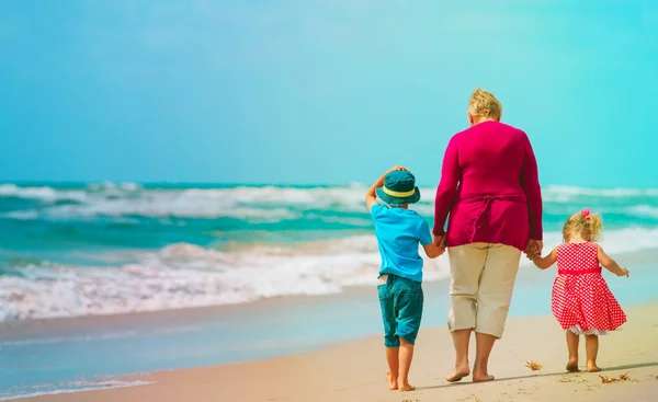 Oma met kinderen - kleine jongen en meisje lopen op strand — Stockfoto