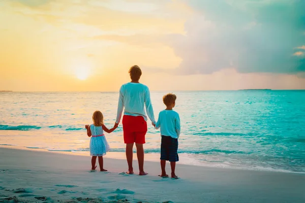 Baba ve iki çocuk gün batımında sahilde yürüyüş — Stok fotoğraf