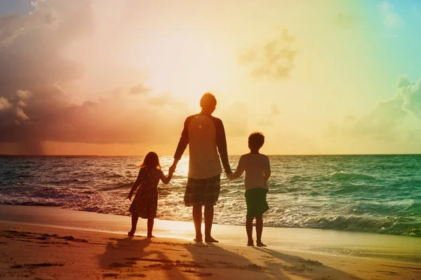 Vader en twee kinderen lopen op het strand bij zonsondergang — Stockfoto