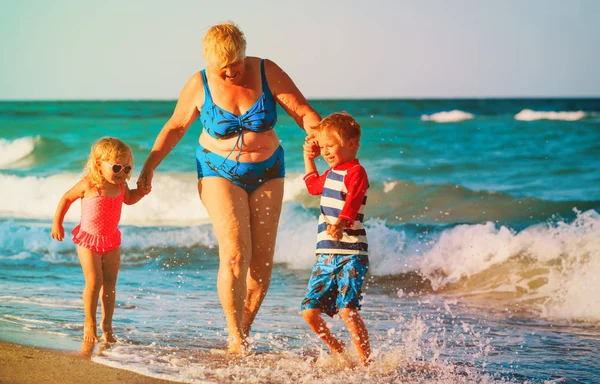Щаслива бабуся з дітьми маленький хлопчик і дівчинка грають на пляжі — стокове фото