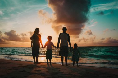 Çocuklu mutlu bir aile gün batımında sahilde yürüyor.