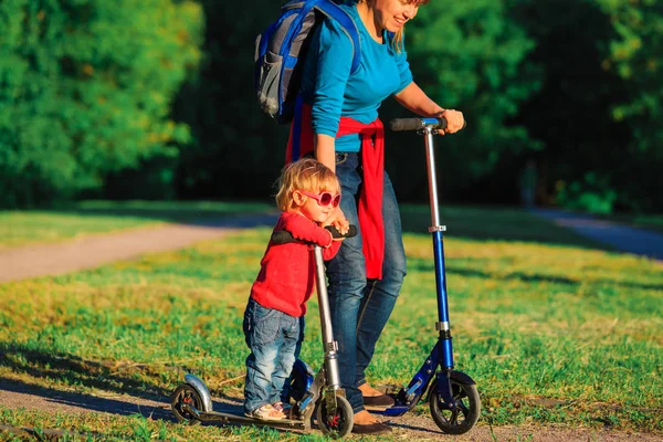 Mãe com pequena filha montando scooters na natureza — Fotografia de Stock