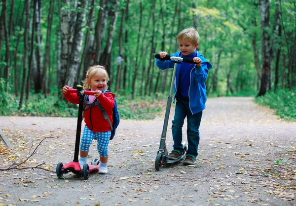 Piccolo ragazzo e bambino ragazza equitazione scooter in natura — Foto Stock