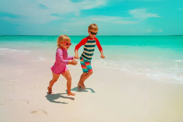 Klein meisje en jongen lopen spelen met water op het strand — Stockfoto