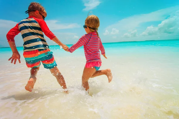 Klein meisje en jongen lopen spelen met water op het strand — Stockfoto