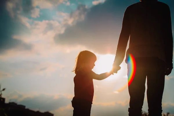 Silhueta de menina segurando a mão dos pais ao pôr do sol — Fotografia de Stock
