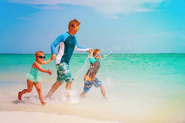 Vader met kinderen spelen met water lopen op strand — Stockfoto