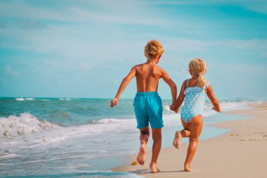 Mutlu kız ve oğlan koşun ve sahilde dalgalarla oynayın