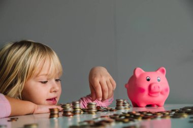 Çocuk para biriktiriyor, tatlı kız domuz kumbarasına bozuk para atıyor.