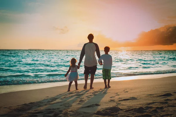 Baba ile oğlu ve kızı gün batımında sahilde yürüyüş — Stok fotoğraf