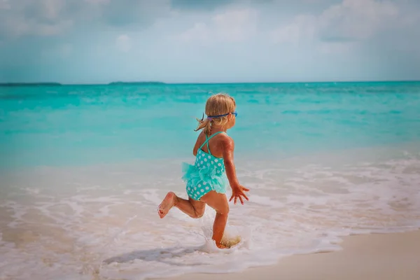 Счастливая маленькая девочка бегает и играет с волнами на пляже — стоковое фото