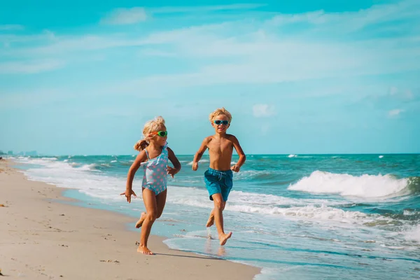 Gelukkig meisje en jongen hardlopen op het strand, kinderen spelen met golven — Stockfoto