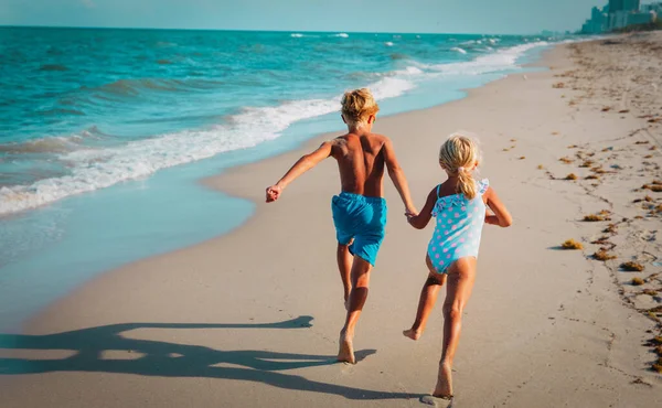 Chica feliz y niño correr y jugar con las olas en la playa —  Fotos de Stock