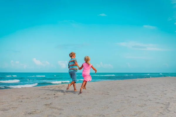 Happy girl and boy run on beach, kids enjoy holiday at sea — Stock fotografie