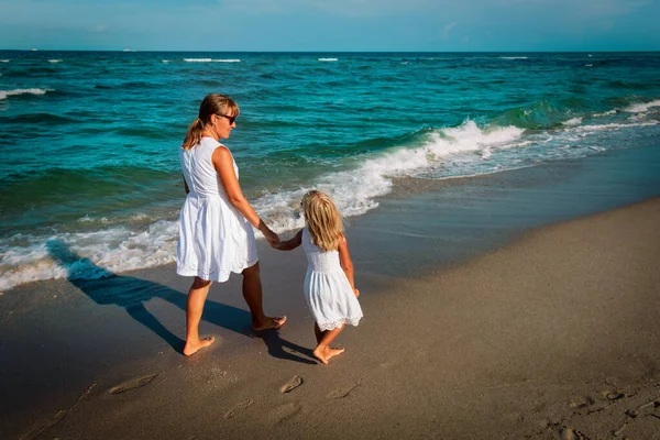 Madre con hija caminando en la playa al atardecer — Foto de Stock