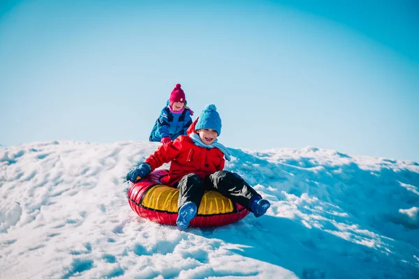 Szczęśliwy ładny chłopiec i dziewczyna slajdów w śniegu zimowym — Zdjęcie stockowe