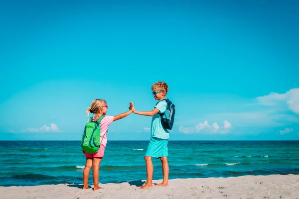 Niños viajan en la playa, niño y niñas con mochila alta cinco en el mar —  Fotos de Stock