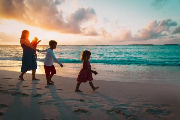 Mãe e crianças andando na praia ao pôr do sol — Fotografia de Stock